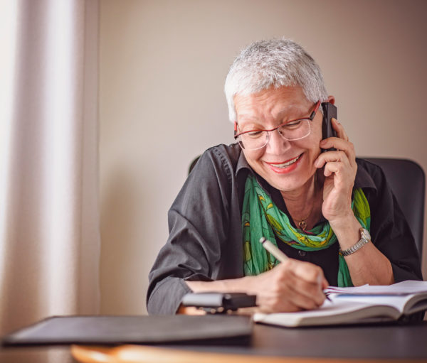 Senior woman drawing a picture in a notebook while taking on cell phone