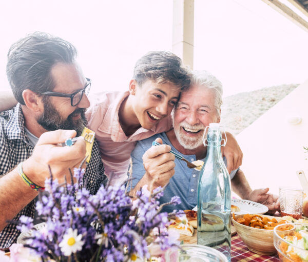 Happy people family concept laugh and have fun together with three different generations ages : grandfather father and young teenager son all together eating at lunch