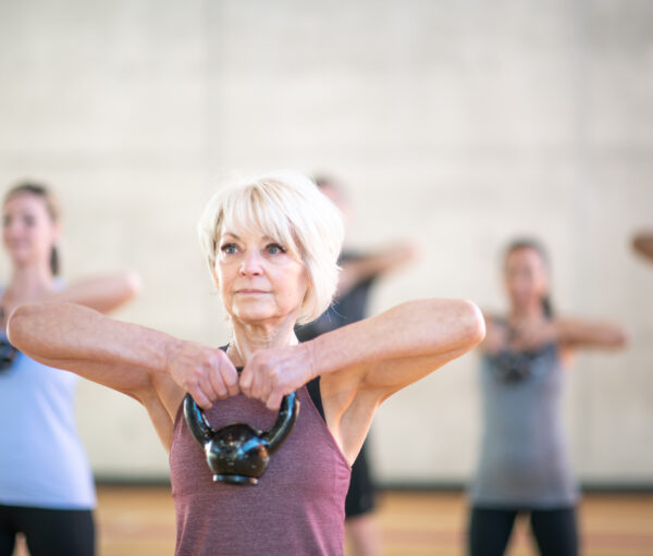 A fit senior Caucasian woman is carrying a dumbbell in her fitness class.
